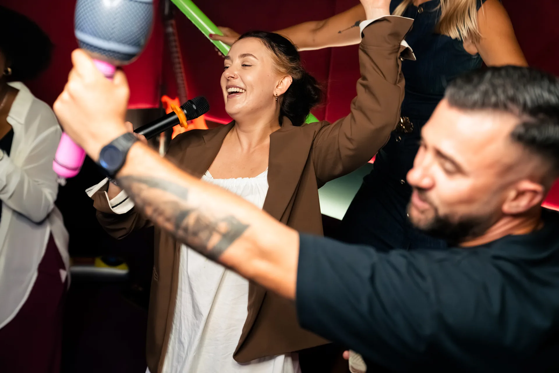 Friends singing karaoke with microphones and inflatable sticks at a lively party
