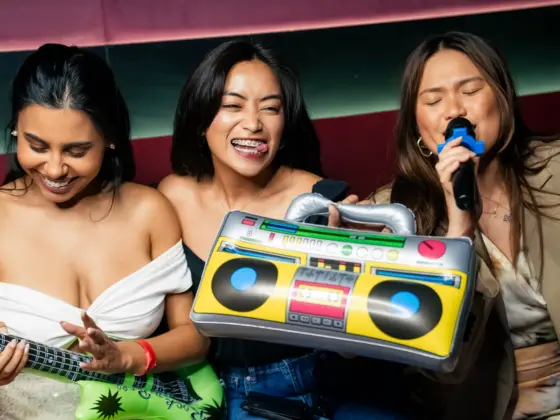 Three friends having fun at karaoke with an inflatable guitar, boombox and microphone