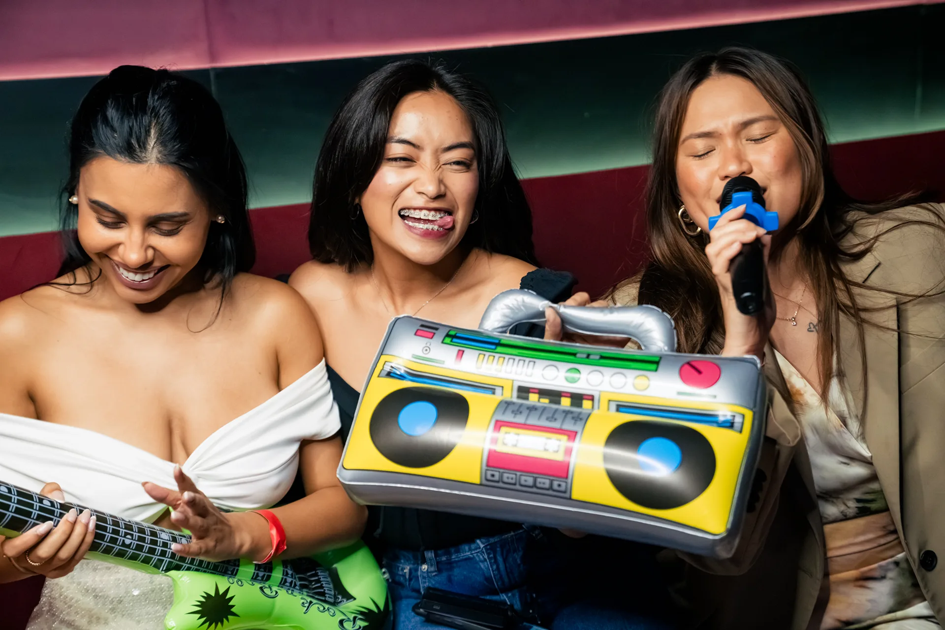Three friends having fun at karaoke with an inflatable guitar, boombox and microphone
