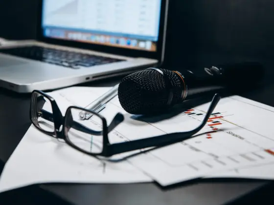 Microphone, glasses and charts on an office desk next to a laptop