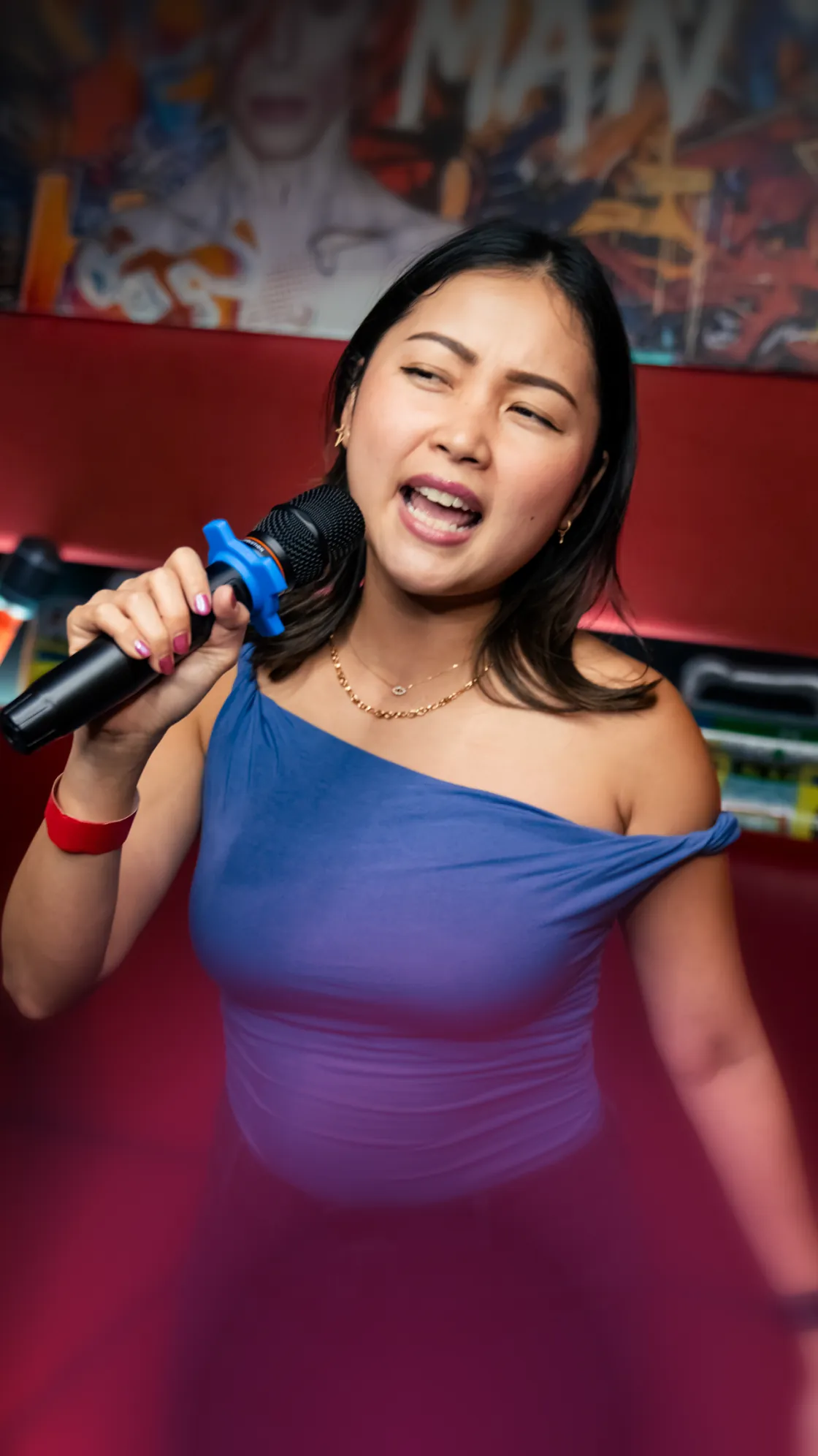Young woman in a blue dress singing into a microphone against colorful graffiti