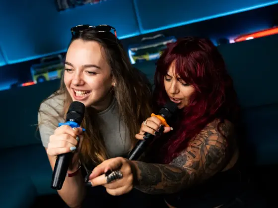 Two young women singing karaoke with wireless microphones in a room with blue lighting