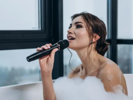 Woman singing into a wireless microphone while relaxing in a bubble bath by the window