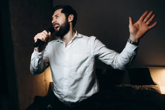 Hombre con barba y camisa blanca cantando con entusiasmo al micrófono de karaoke en casa