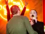 Woman singing into a microphone at a karaoke party as guests raise rock horns in front of a neon sign