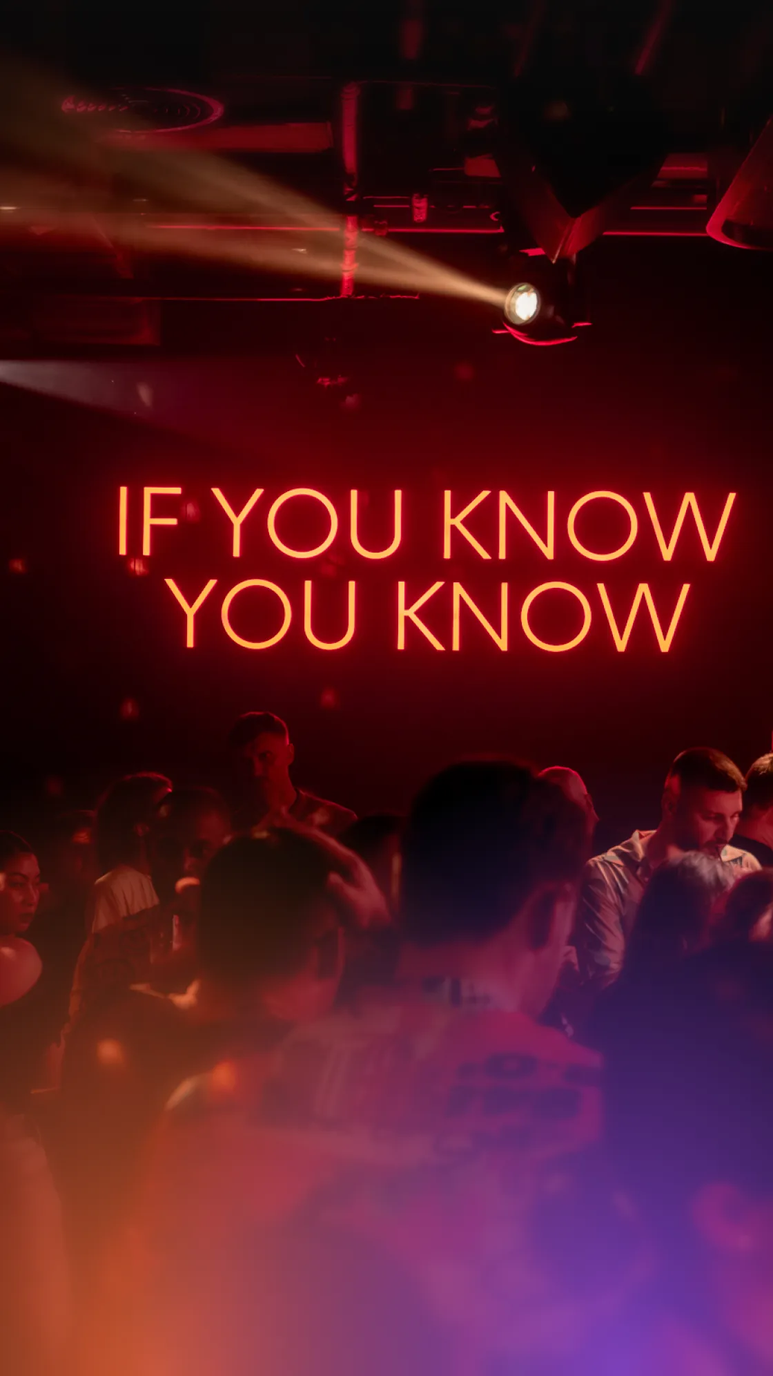Neon sign reading “If you know you know” above karaoke club guests