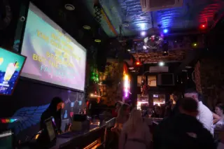 A karaoke club hall with a big lyrics screen, a bar counter, a disco ball and guests with a microphone