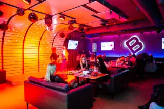 Karaoke club hall: a stage with disco balls, neon lighting and guests at tables on sofas