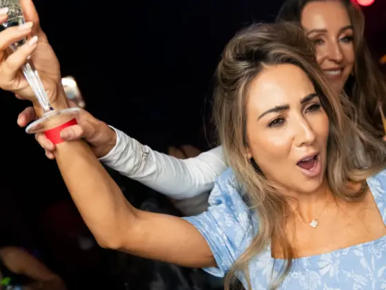 A woman in a light blue dress singing and raising a glass with friends at a karaoke club party