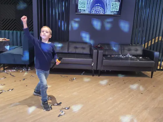 A boy with a microphone happily raising his fist at a kids’ party in a karaoke room with confetti on the floor