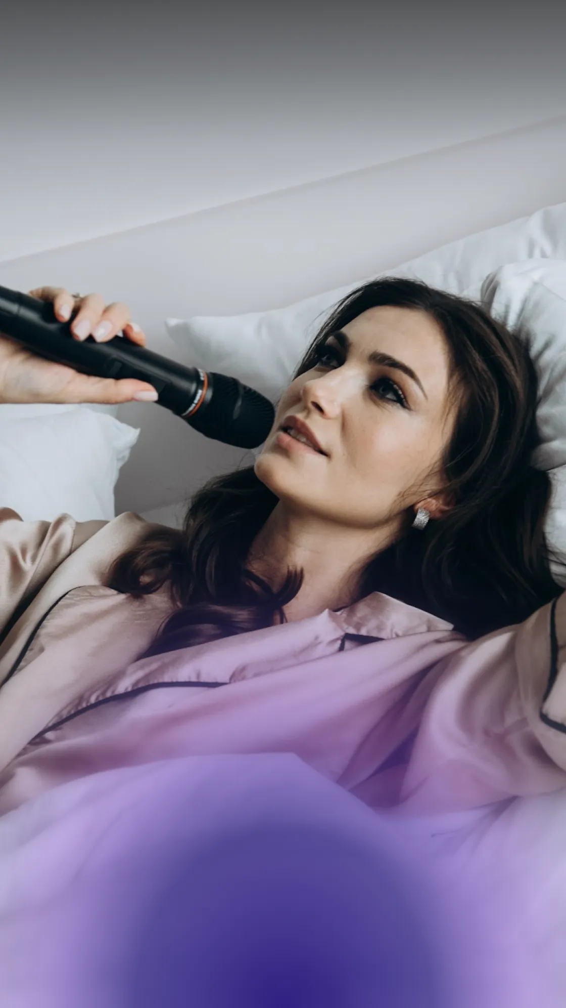 Close-up of a brunette on a white pillow singing into a microphone