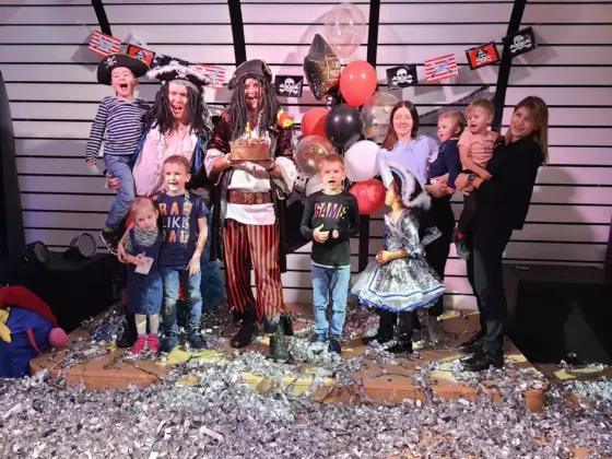 Kids and parents with pirate entertainers and a cake on stage at a children’s party among confetti