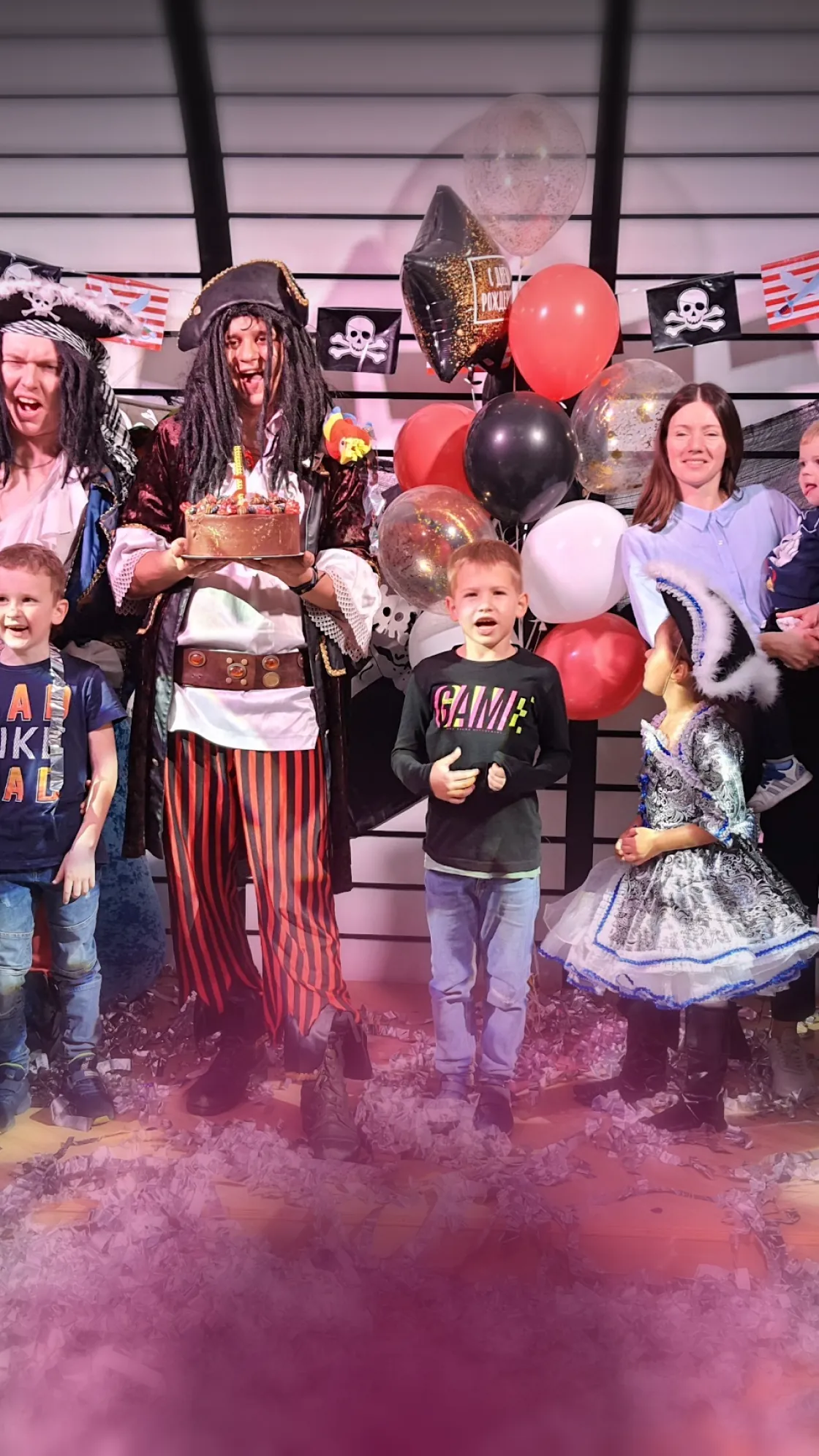 Pirate entertainer holding a birthday cake with kids in costumes at a party