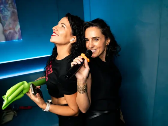 Two friends with a microphone and an inflatable guitar happily singing in a karaoke room with blue lighting