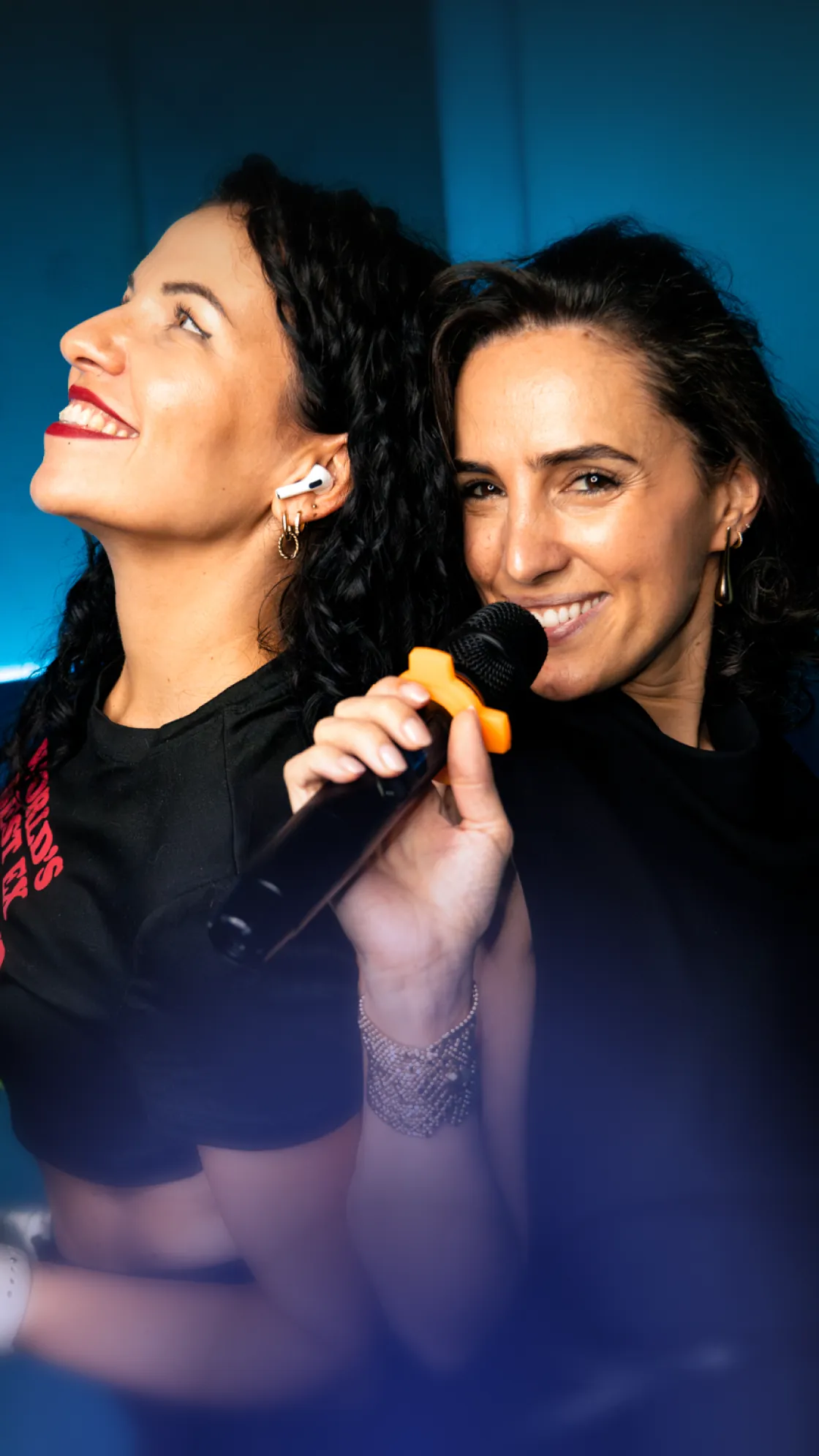 Two smiling friends singing into a microphone with an orange grip