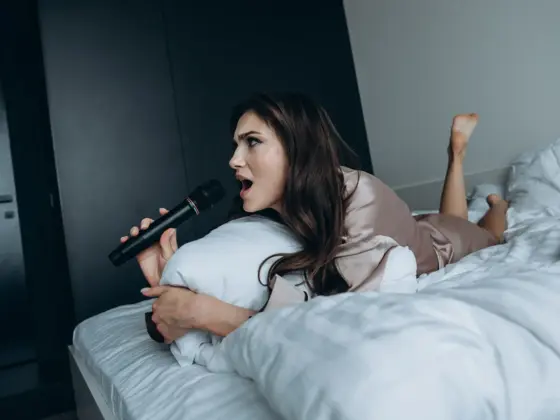 Una chica en pijama de seda tumbada en la cama canta con un micrófono por la mañana en casa