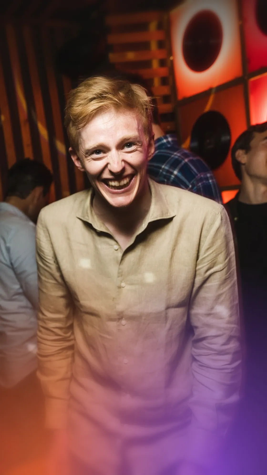 Red-haired young man in a linen shirt laughing at a karaoke bar party