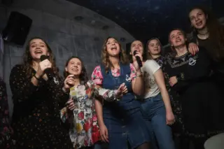 A group of young women joyfully singing into microphones in a karaoke room with a starry ceiling