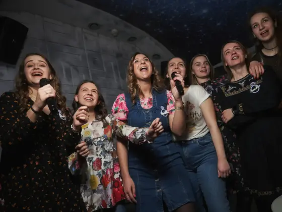 A group of young women joyfully singing into microphones in a karaoke room with a starry ceiling