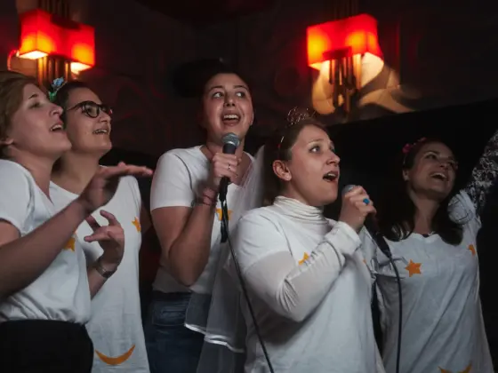 A bride in a veil and her friends in matching star T-shirts singing into microphones at a karaoke hen party