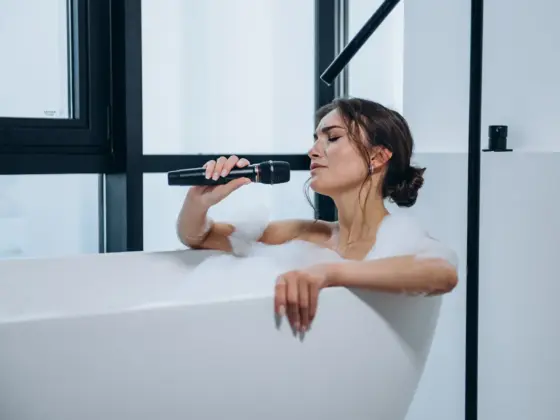 Young woman singing into a microphone while relaxing in a bubble bath by a large window