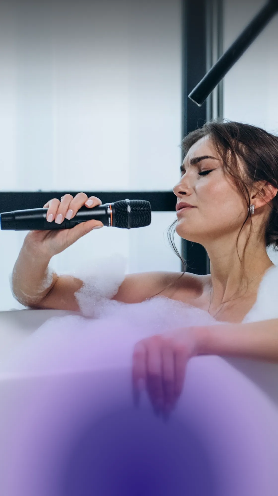 Young woman with closed eyes singing into a microphone in a bubble bath