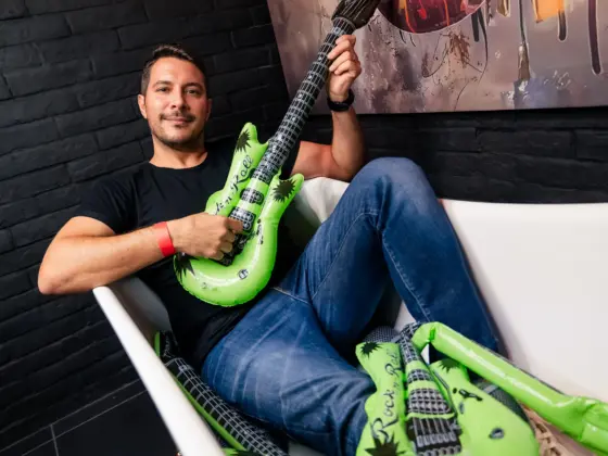 A smiling man sitting in a white armchair holding a green inflatable guitar