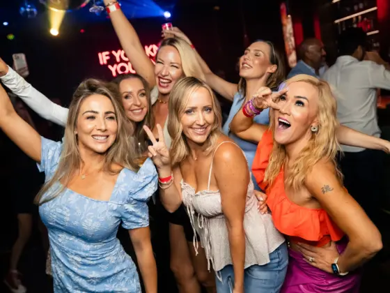 Group of girlfriends happily posing and dancing at a bachelorette party in a karaoke bar