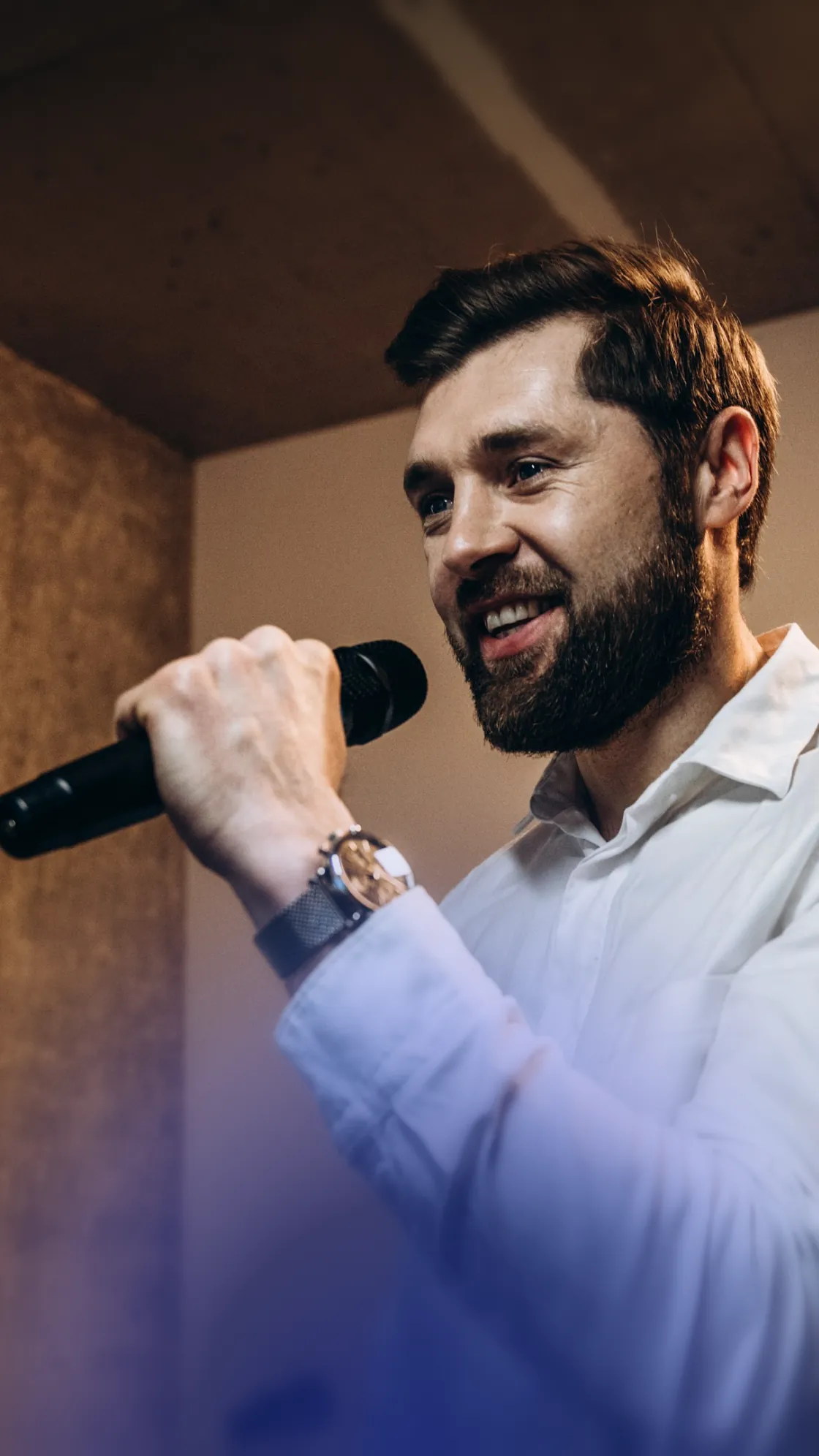 A bearded man in a white shirt smiling and singing into a microphone